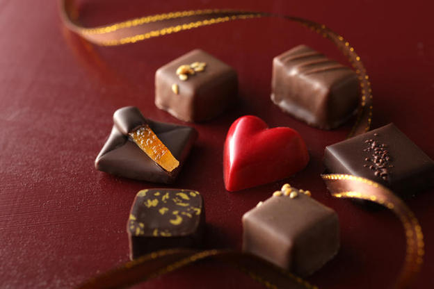 赤い背景に置かれたさまざまな種類のプラリネとハート型のチョコレート