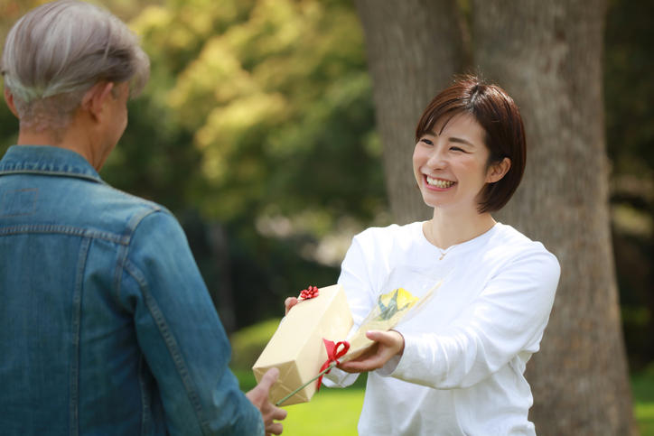年配の男性へプレゼントを手渡しする若い女性