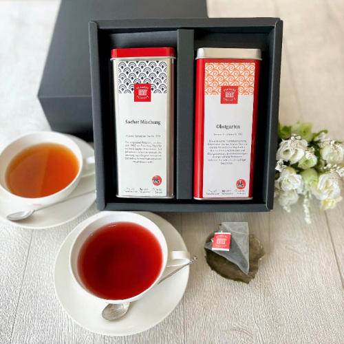 茶葉缶が2つ入った黒色のギフトボックスと、紅茶が入ったティーカップが2つ置かれている。