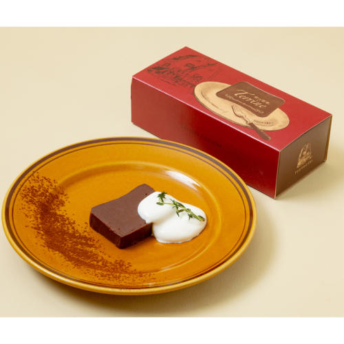 茶色い皿の上にカットされたテリーヌショコラが盛られており、その横には赤い箱が置かれている