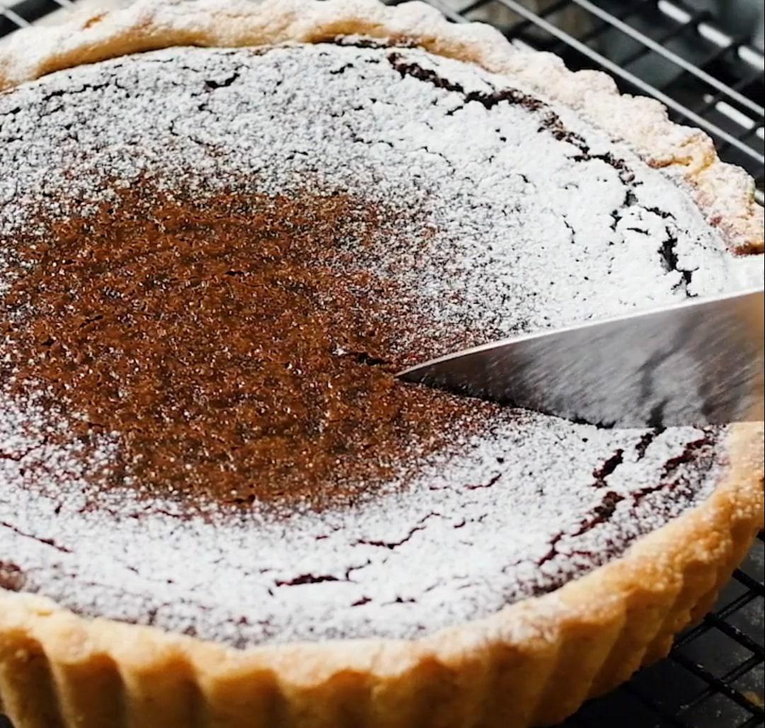 クローズアップされた粉糖がかかったチョコタルトに包丁の刃が入っている様子