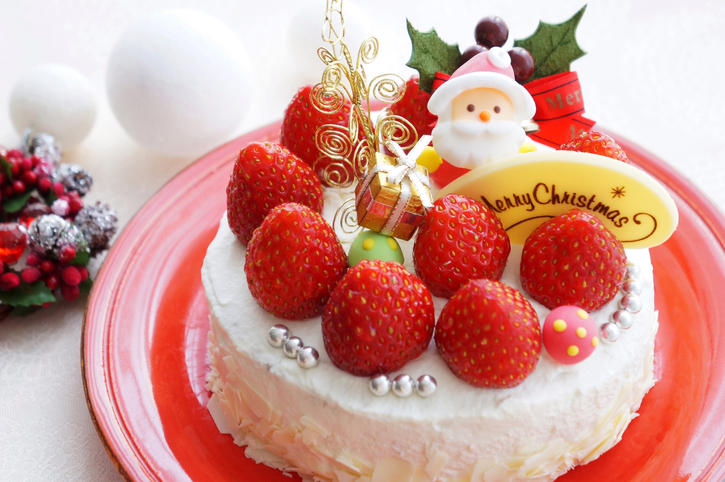 トップにサンタクロースといちごが飾られたホールタイプのショートケーキが赤色の皿にのっている。