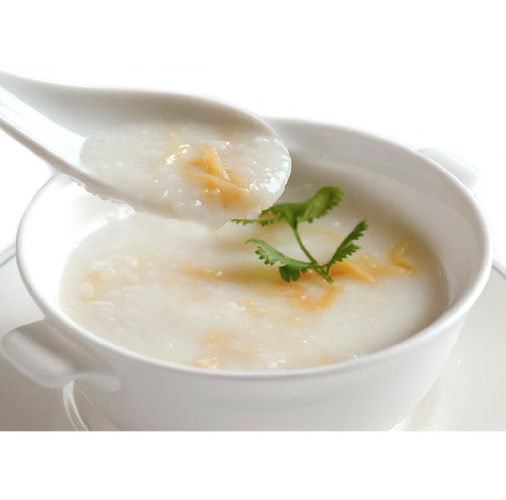 白い陶磁器のスープカップに入ったお粥をすくいあげる蓮華
