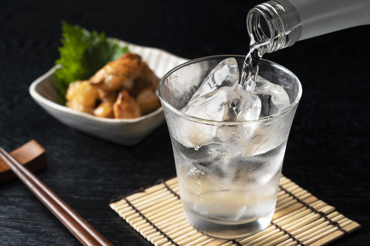 グラスに注がれた焼酎と後ろにある白い器に盛られたおつまみ