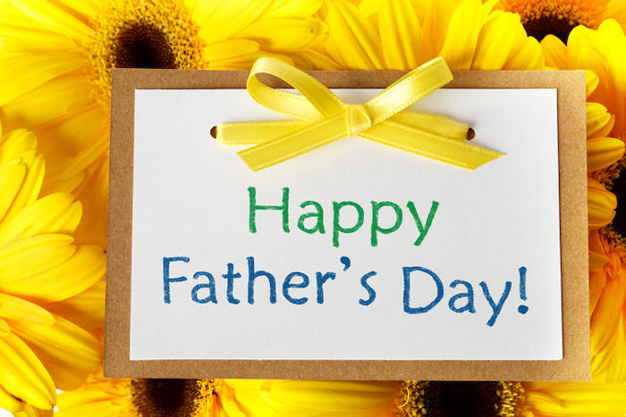 黄色の花を背景に、黄色のリボン付きの、Happy Father's Day!と書かれたメッセージカードが置かれている