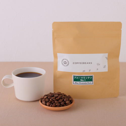 テーブルの上に、コーヒーが入ったマグカップ、コーヒー豆、茶色の袋が置かれている。