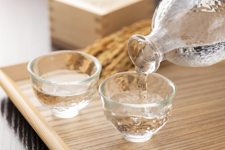 木製のトレーの上で2つのグラスに日本酒を注いでいる様子