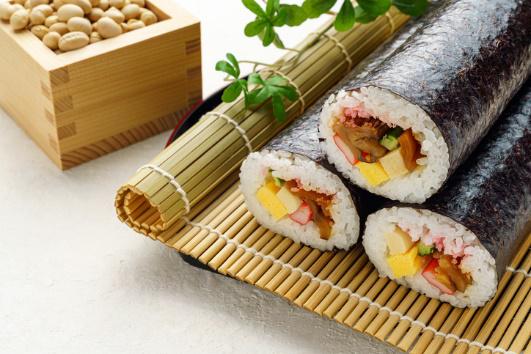 枡に入った大豆と巻きすにのった3本の太巻き寿司