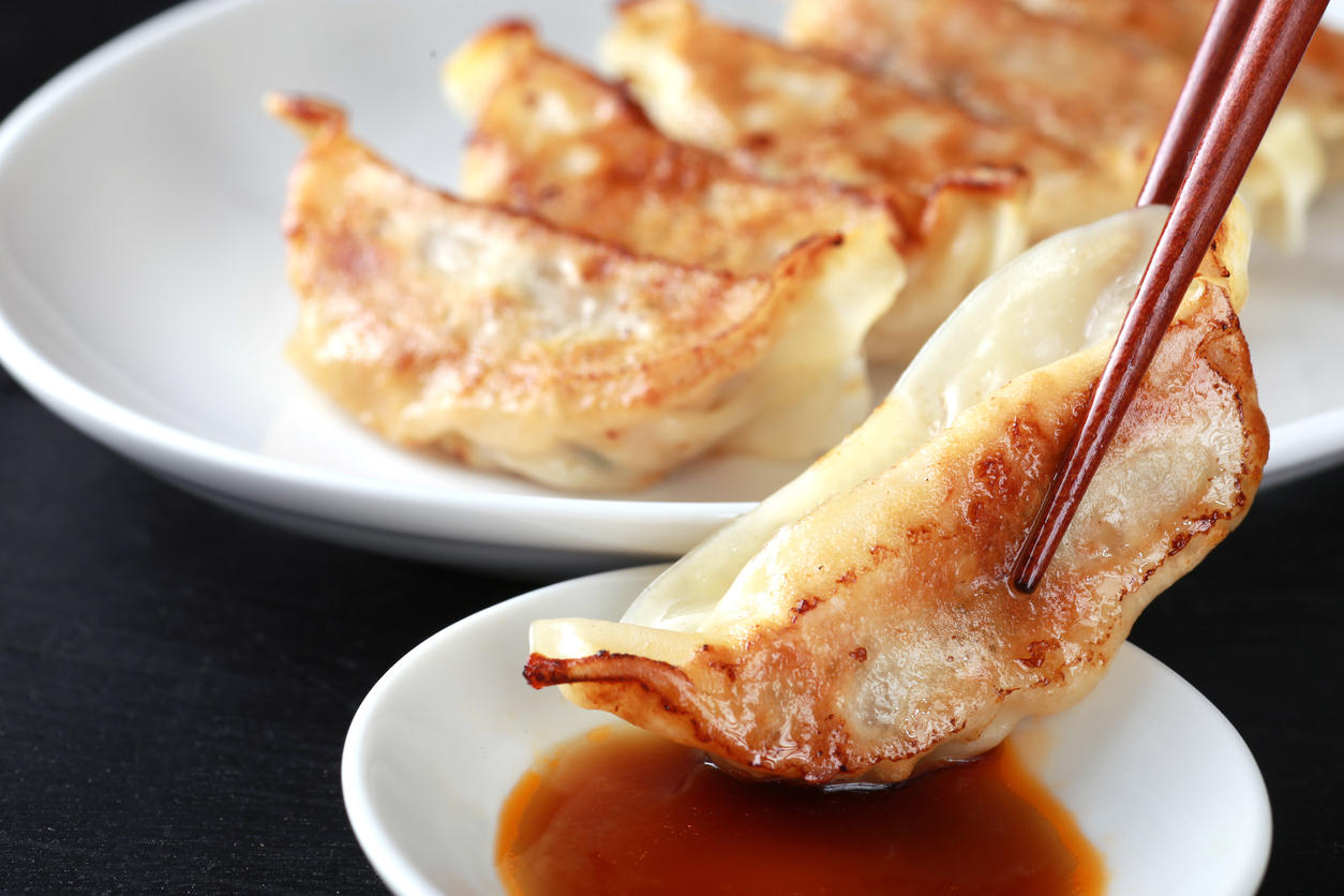 タレが入った小皿に焼き餃子を浸している