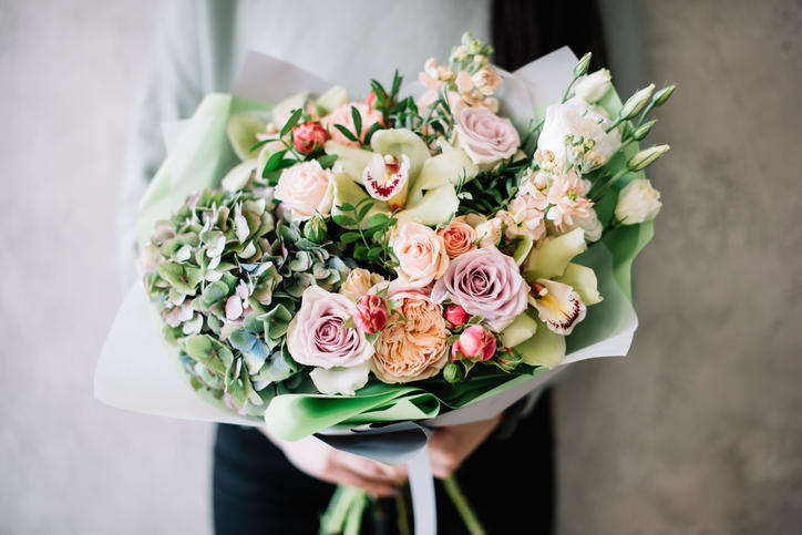 灰色の壁を背景に、女性が花束を持っている。