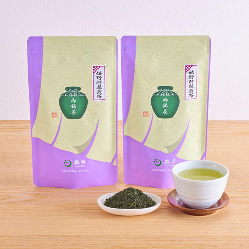 煎茶が入った湯呑み、茶葉が盛られた白い皿、茶葉のパッケージが2つ置かれている。