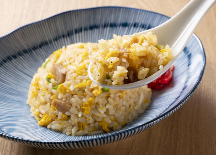 青色の器に入った炒飯をレンゲですくっている。