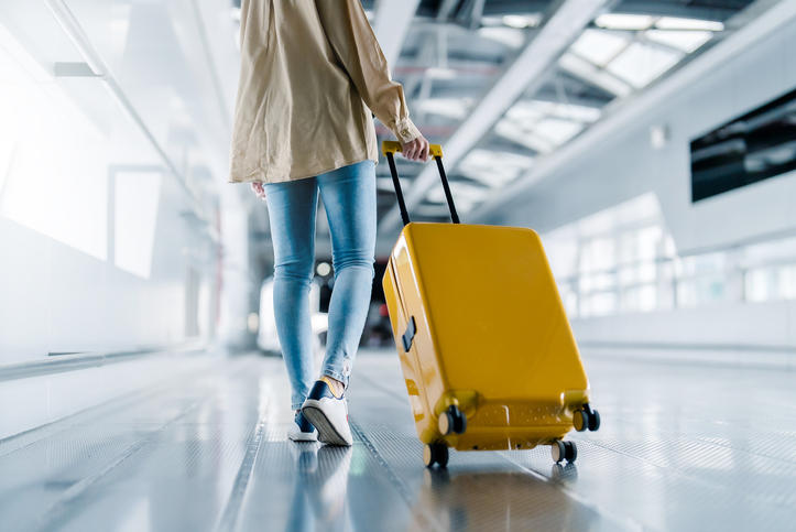オレンジ色のスーツケースをひいて空港を歩く女性。