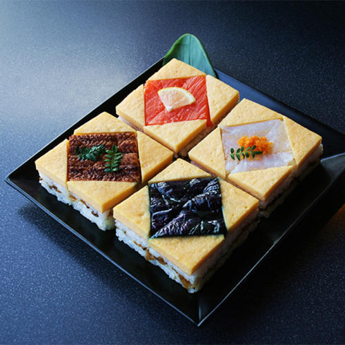 黒く四角い器のなかに錦糸卵やサーモンなどがのった蒸し寿司が４種類つめられている