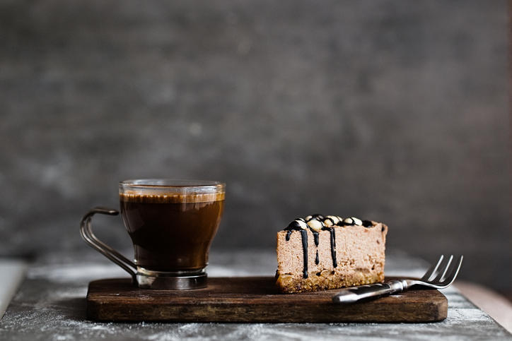 グレーの背景に置かれた木の板の上のケーキとカップ入りコーヒー