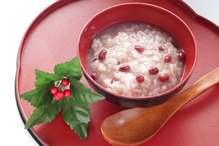 赤色のお盆に、小豆粥を盛ったお椀とスプーンが置かれている。