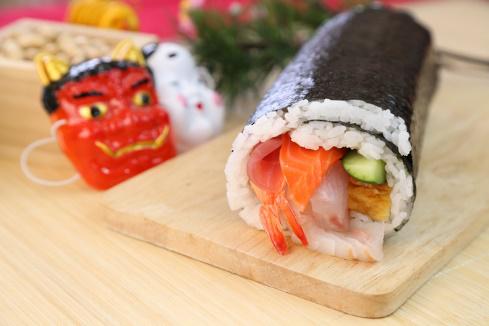 鬼とお多福の面の横に板皿に盛られた恵方巻きが置かれている様子