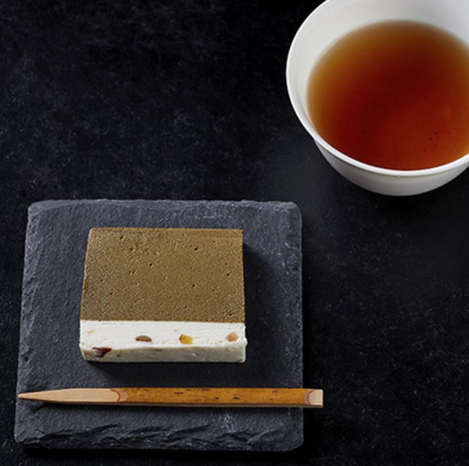 黒い背景に置かれた白い湯呑みのなかのお茶と黒い皿の上のテリーヌのスライスと竹楊枝