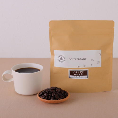 ベージュのテーブルに置かれた白いカップ入りのコーヒーと小皿に盛られたコーヒー豆、紙袋
