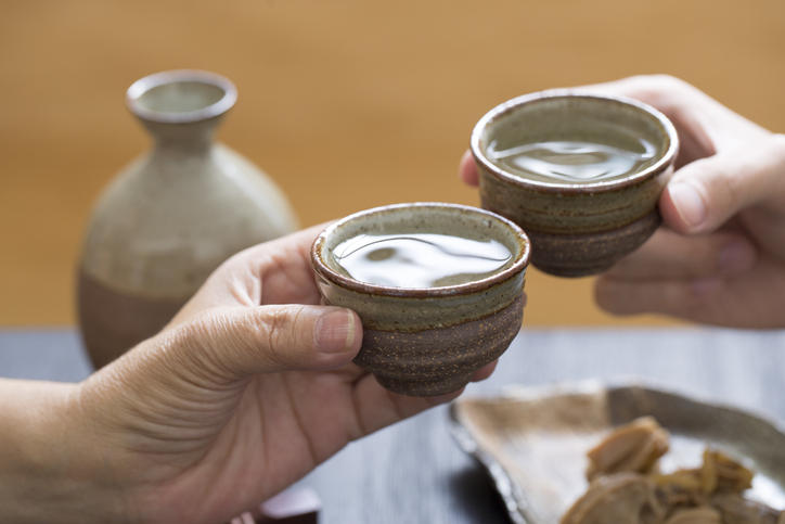 お酒が入ったお猪口を手に持ち乾杯する様子