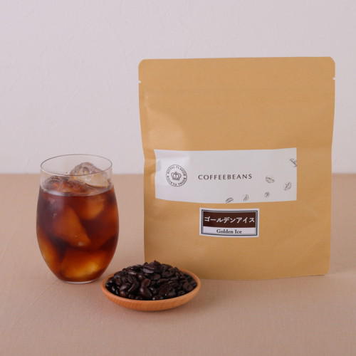 テーブルに、コーヒー入りのグラス、コーヒー豆、茶色の袋が置かれている。