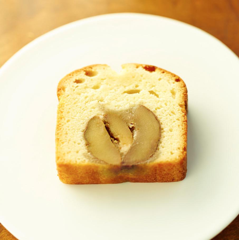 木製のテーブルに置かれた白い丸皿の上の一切れの栗入りパウンドケーキ