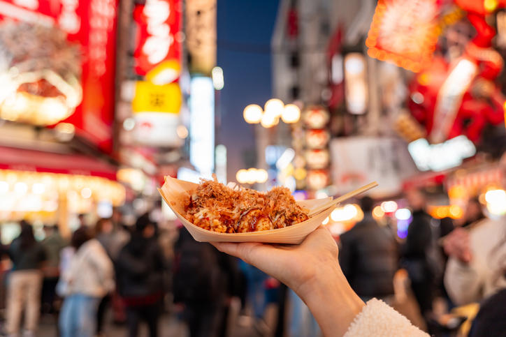 大坂の街並みを背景にたこ焼きを持っている様子