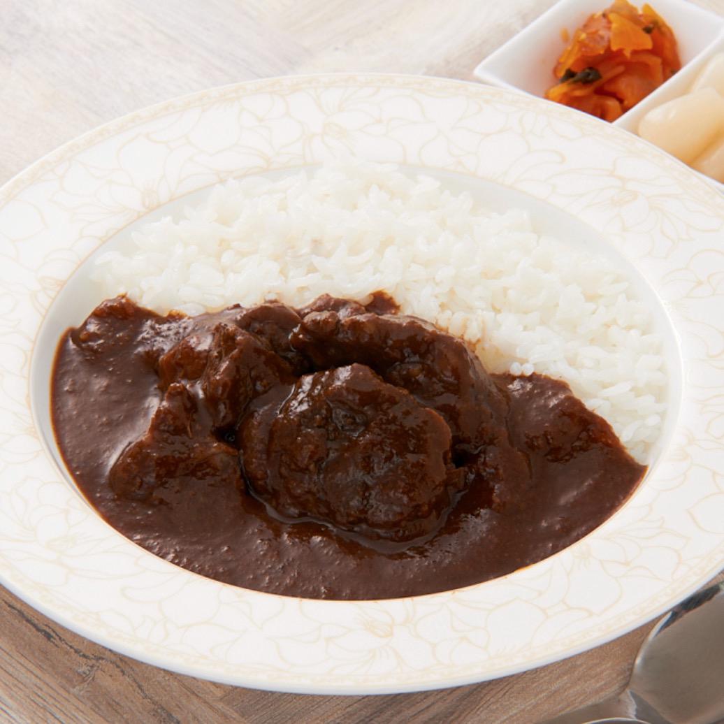 テーブルの上に置かれたカレーライスが入った白い丸皿と福神漬けなどの小皿