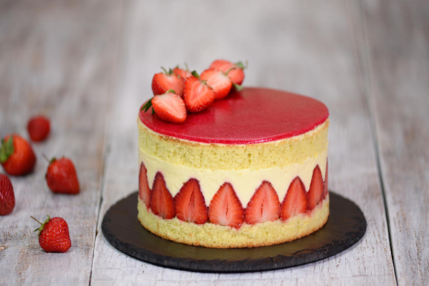 表面と側面にいちごを飾ったホールケーキが黒色の皿に置かれている。