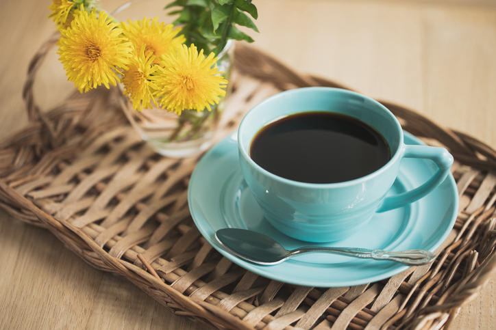青いマグカップに淹れられたコーヒーにたんぽぽが添えられている