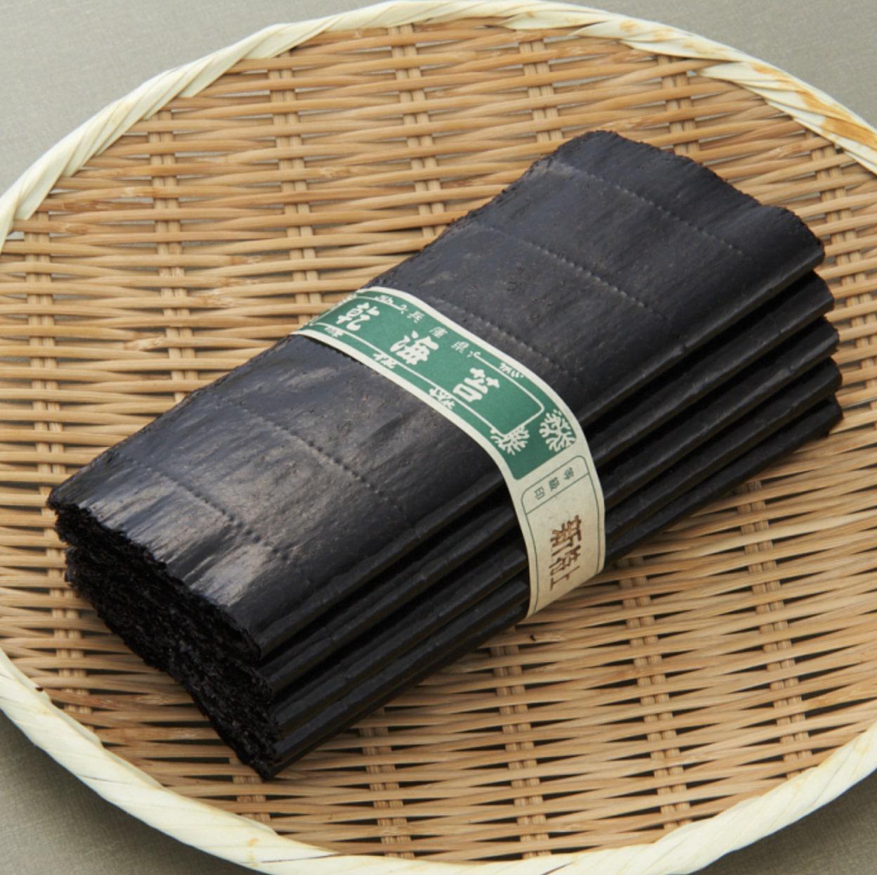 グレーの背景に置かれた竹かごの上の帯留めされた束の焼きのり
