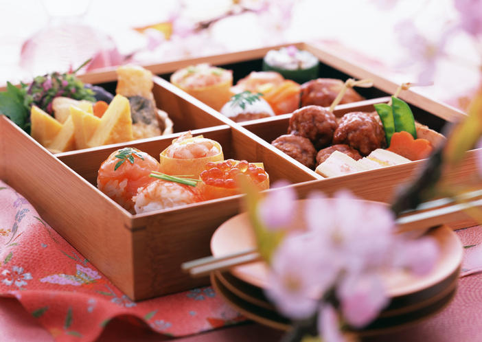重箱にさまざまな食べ物が詰められていて、手前に桜の花が見える