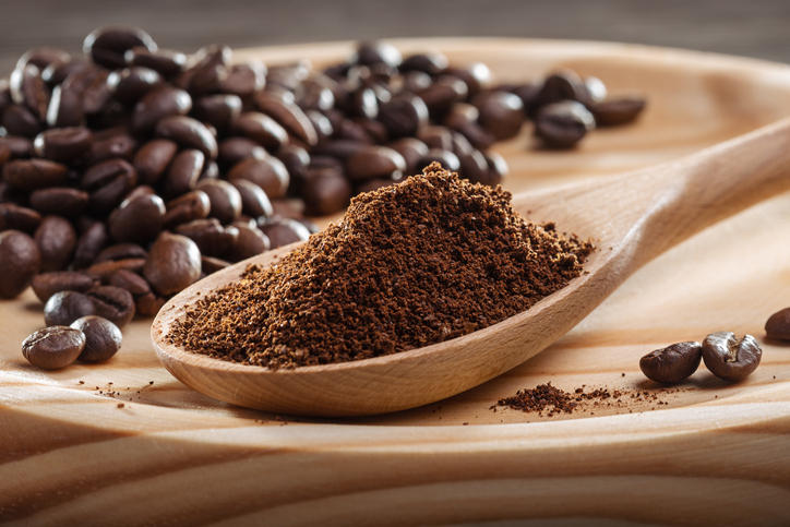 コーヒー豆を背景に木製スプーンにコーヒー粉が盛られている