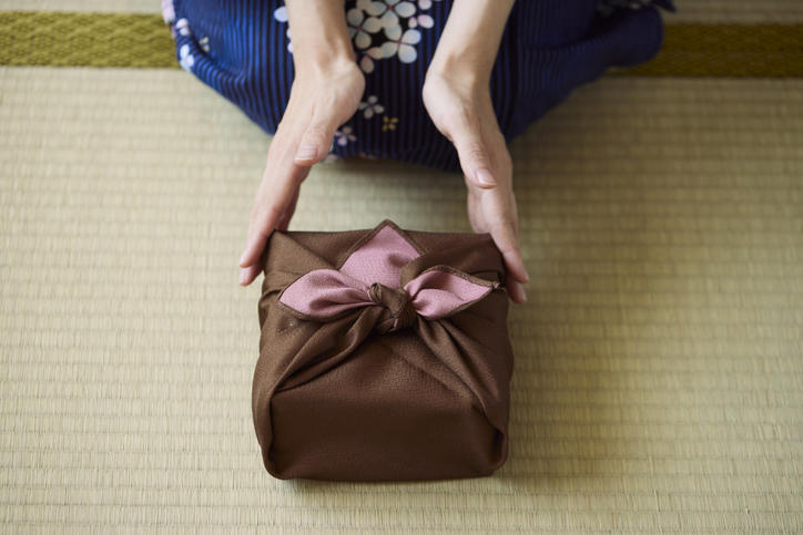 畳の上で茶色いギフトを差し出す浴衣を着た女性の手