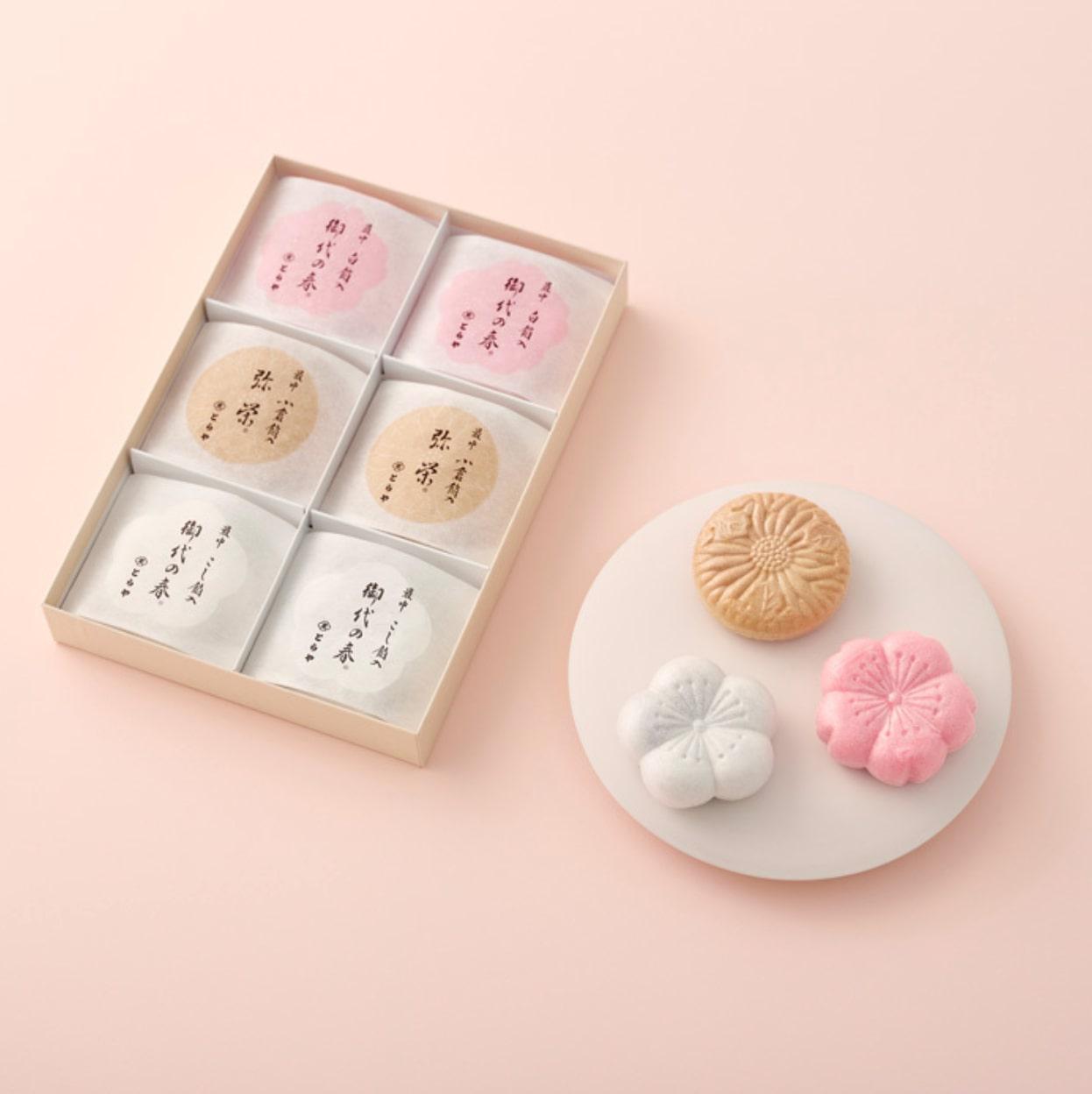 淡いピンクの背景に置かれた白い丸皿の上の白・ピンク・茶色のもなかともなかの入ったボックス