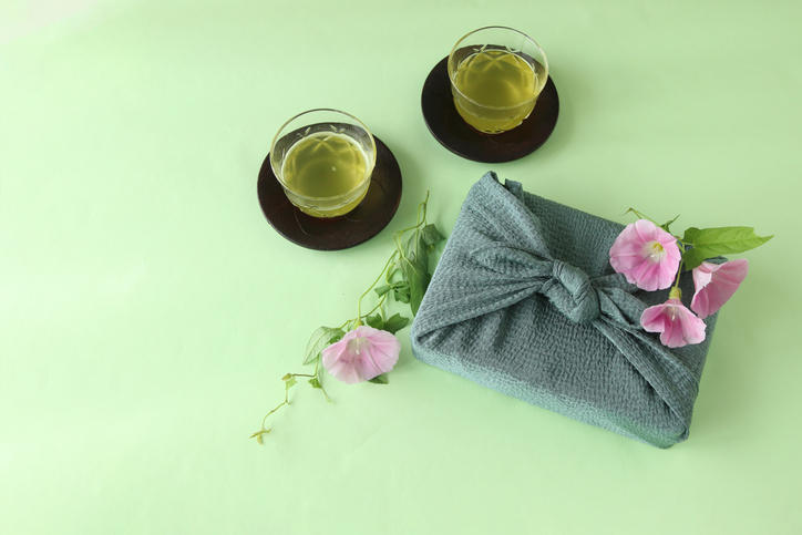 青い風呂敷に包んだギフトと花、傍らに冷茶2杯が置かれている