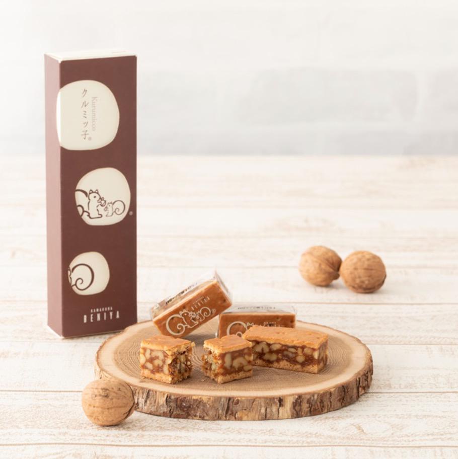 木目調の背景に置かれた輪切りの木の板の上のくるみのお菓子と立てられた茶色い箱