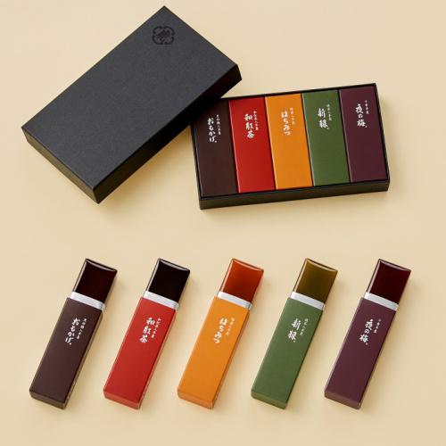 手前にステイックタイプの羊羹が5本並び、奥には羊羹が5本入った黒色のギフトボックスが置かれている。