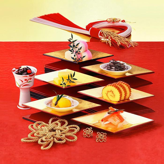 赤と金の背景に置かれた四角い皿の上のおせち料理の数々