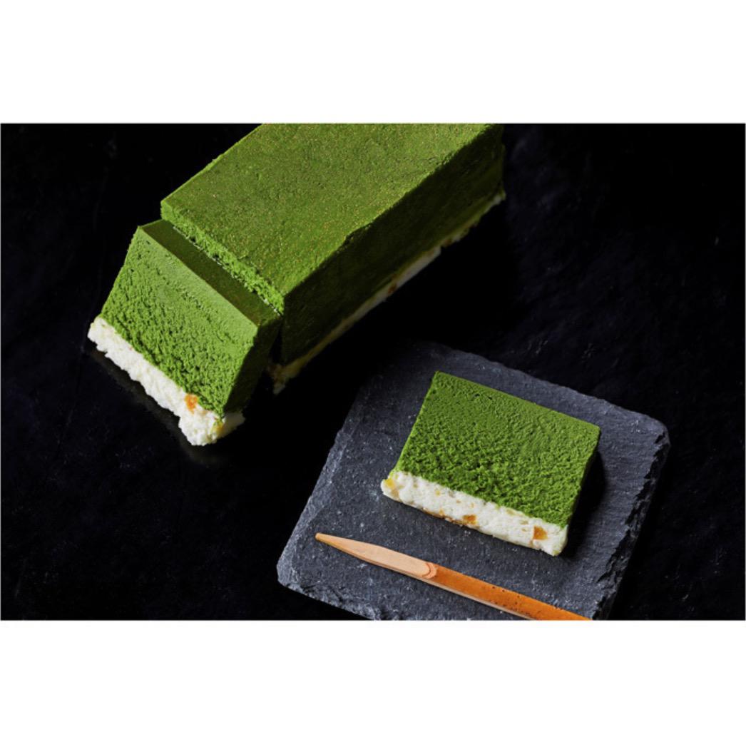 黒い背景に置かれた1本の抹茶テリーヌと黒い四角い皿の上のスライスされた抹茶テリーヌと竹楊枝