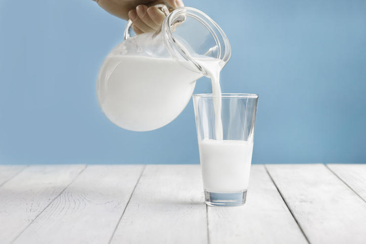 白い台の上でデキャンタからグラスに牛乳が注がれている