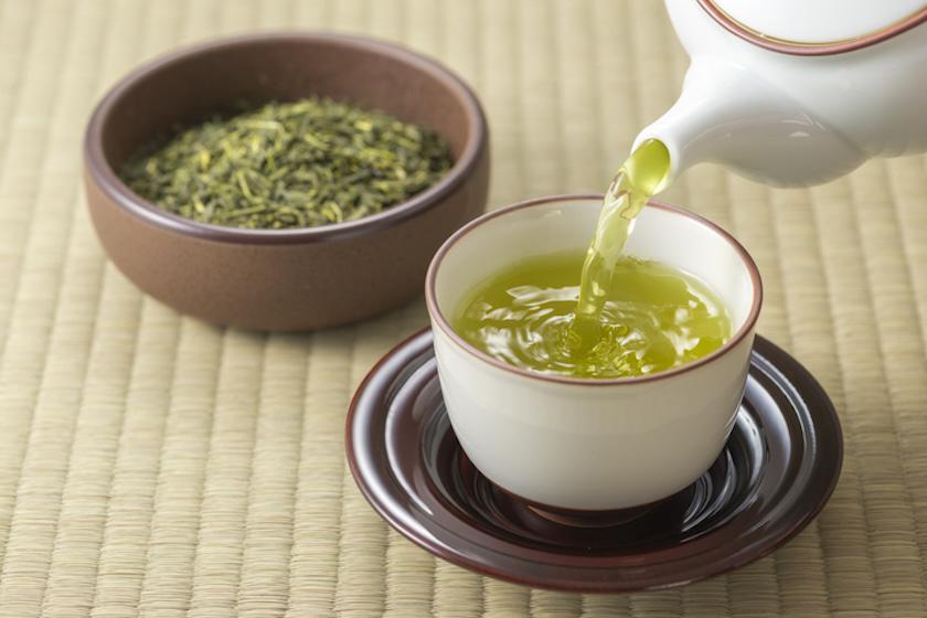 畳の上で湯呑みに緑茶を注いでいる。