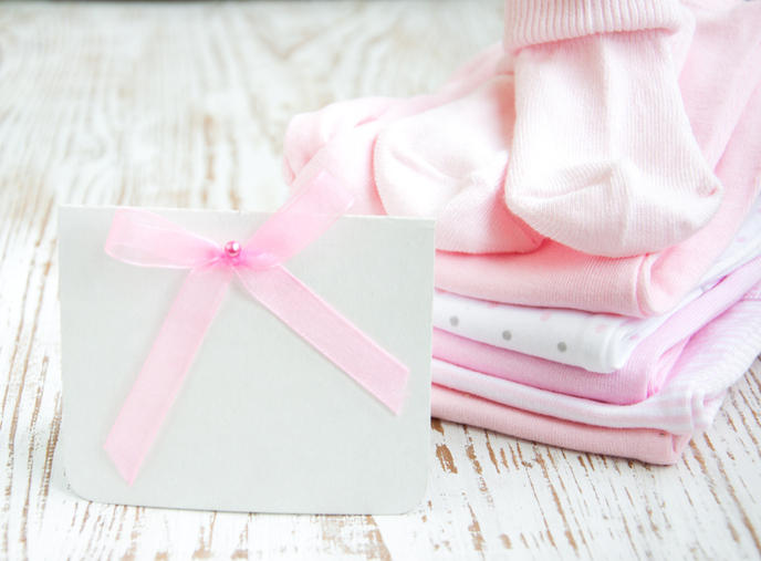 ピンク色のリボンを付けたメッセージカード、傍らにベビー服と靴下