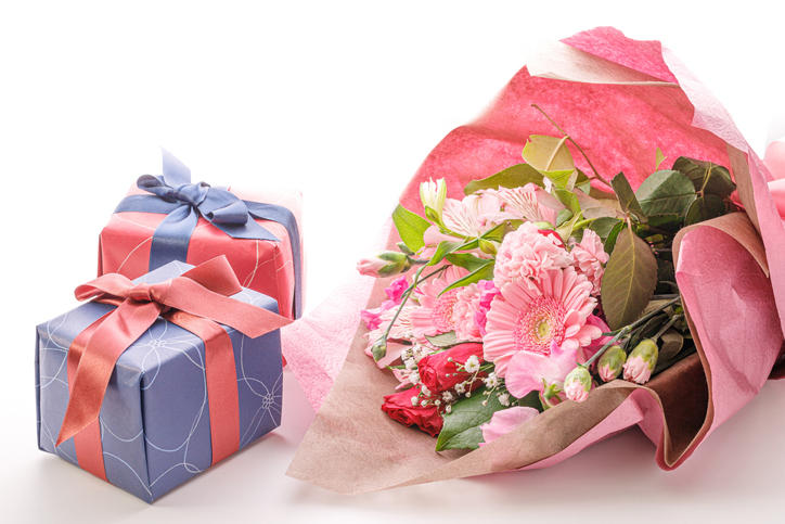 ピンクのラッピングペーパーで包まれた花束と、ブルーとレッドの包装紙で包まれたふたつのギフトボックス