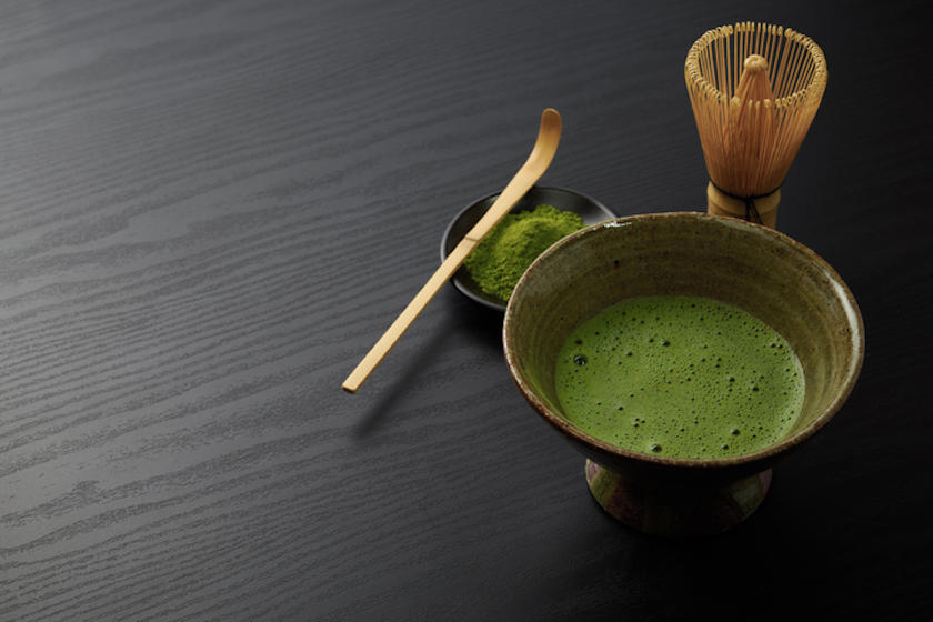  黒色の背景に、抹茶碗、茶しゃく、抹茶、茶せんが置かれている。
