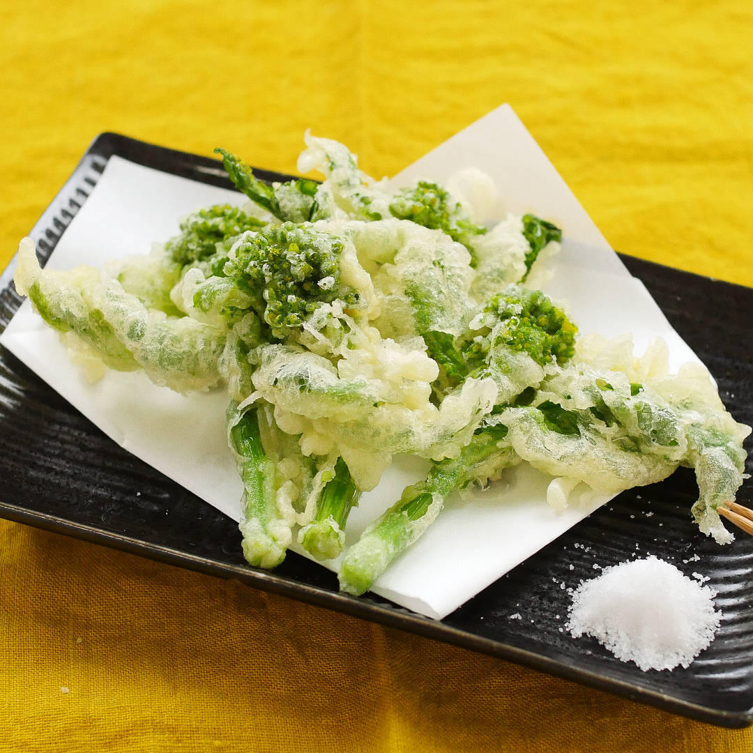 黒の皿に盛られた菜の花の天ぷら