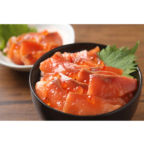 木製テーブルの上の黒い丼に盛られた鮭丼