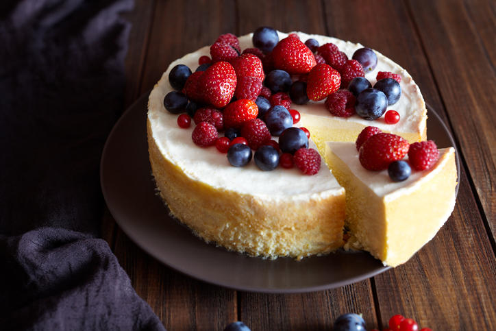 ひとり分カットされたいちごやブルーベリーが乗ったホールのチーズケーキ