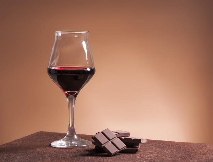 茶色の背景に、赤ワインが入ったグラスとチョコレートが置かれている。