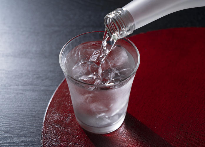 赤いお盆に置かれたグラスに焼酎をそそいでいる